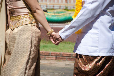 Midsection of couple holding hands while standing on footpath