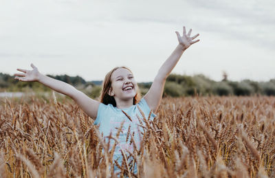 Happy woman with arms raised on field against sky