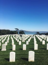 Tombstones in cemetery against clear blue sky