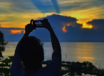 Rear view of man photographing sunset through mobile phone