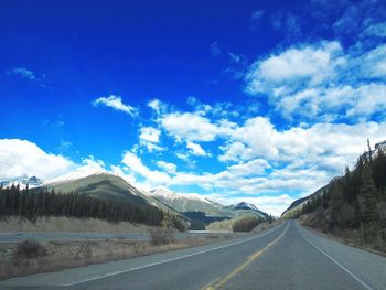 Empty road leading towards mountains against blue sky