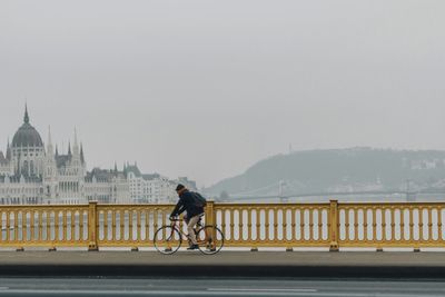 Man riding bicycle on bridge against sky