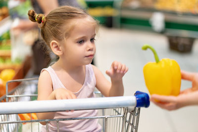 Cute girl receiving yellow bell pepper at supermarket