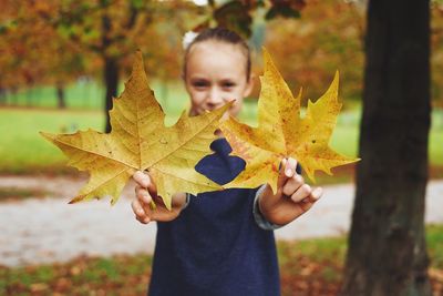 Girl holding autumn leaves in park