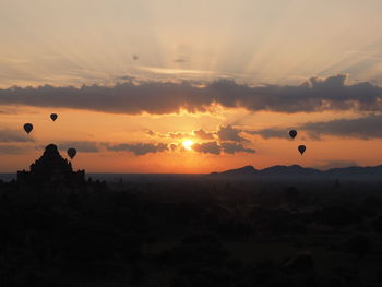 Silhouette hot air balloons flying over ancient temples against sky during sunset