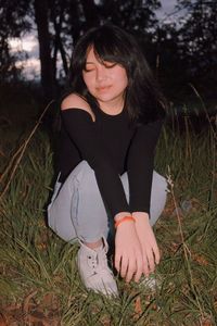 Full length of woman sitting on grass during dusk