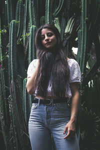 Portrait of young woman with long hair standing against plants
