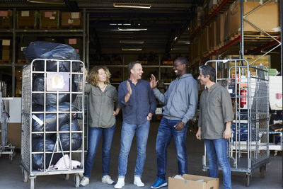 Full length of cheerful coworkers standing amidst carts at warehouse doorway