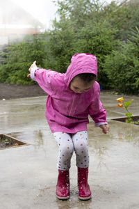 Girl wearing raincoat splashing in puddle