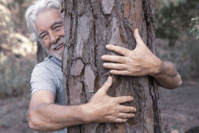 Portrait of smiling man holding tree trunk while standing outdoors