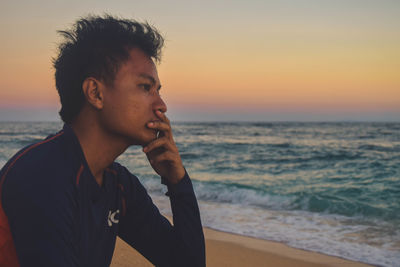 Portrait of man looking away at beach against sky during sunset