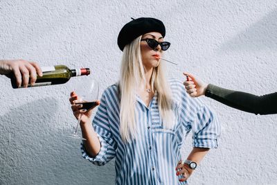 A young girl in a beret and glasses holds a glass with red wine and a cigarette