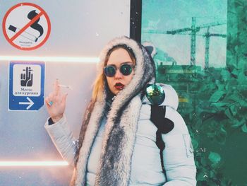 Woman in warm clothing holding cigarette by information sign