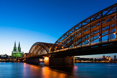 Illuminated bridge over river against blue sky at night
