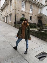 Portrait of teenage girl standing on footpath against building