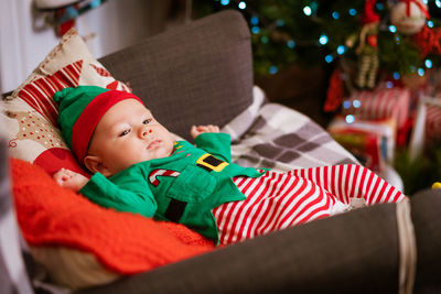 Beautiful half-year-old child lies on pillows and smiles in a red-green costume