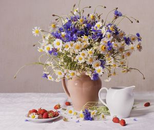 Flower vase with strawberries in plate on table against wall