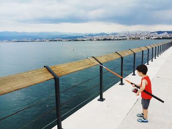 Boy fishing in sea against sky