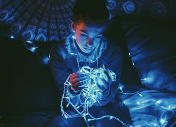 High angle view of woman with illuminated string lights in darkroom