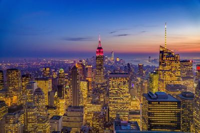 Illuminated empire state building amidst buildings at manhattan