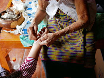Midsection of senior woman tying string on granddaughter hand