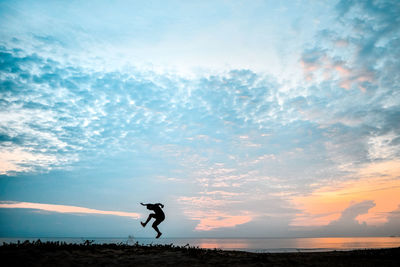 Silhouette man jumping at beach against sky during sunset