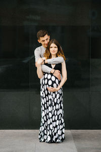 The husband embraces his wife and keeps her hand on her pregnant belly
