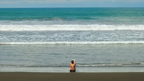 Rear view of woman sitting at beach during sunny day