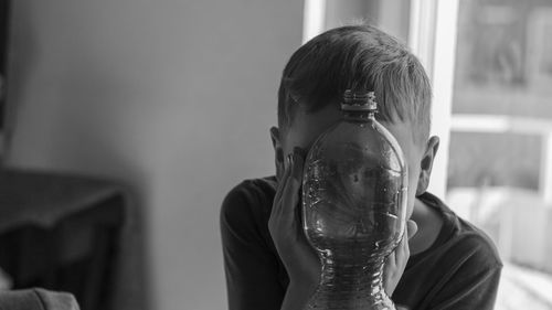 Boy hiding face behind bottle at home