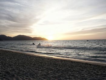 Silhouette person riding jet boat in sea against sky during sunset