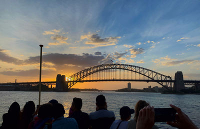 People on bridge over sea against sky during sunset