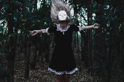 Woman wearing mask with arms outstretched standing in forest