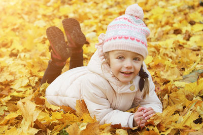Portrait of smiling cute girl lying down on leaves during autumn