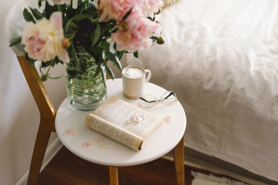 Open book with glasses, cup coffee and bouquet white pink peonies flowers. read and rest. cozy home