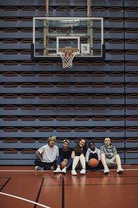 Full length portrait of boys and girls sitting together in basketball court