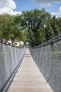 Narrow footbridge along trees and plants against sky