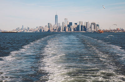 Wakes in river against cityscape