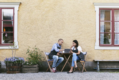 Bakers discussing over digital tablet while sitting at table outside cafe