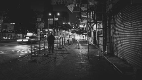 Man standing on sidewalk by road in city at night