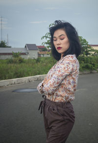 Young woman looking away while standing on road in city