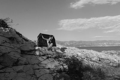 Rear view of man standing on rock by sea against sky