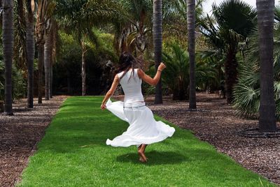 Rear view of woman dancing on grassy pathway by palm trees