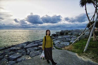 Woman with plastic bag standing on rock by sea against sky