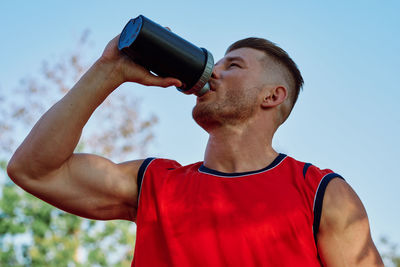 Close-up of man holding bottle against sky