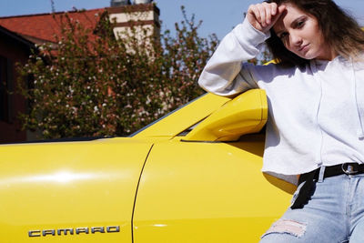 Mid adult woman standing by yellow car