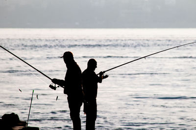 Silhouette man fishing by sea against sky