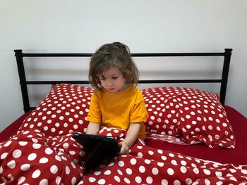 Girl using digital tablet while sitting on bed at home