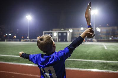 Young soccer player in blue jersey with ten number raising a trophy after the winning goal