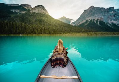 Rear view of woman sitting in boat on lake against mountains