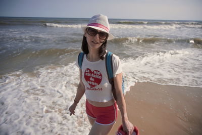 Young woman standing at beach against sky